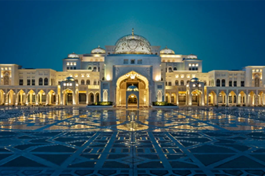 A wide evening shot of the Qasr Al Watan presidential palace in Abu Dhabi, showcasing its white granite facade and grand domes reflecting in the polished courtyard tiles.