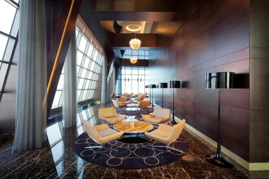 A bright, modern seating area at the Observation Deck at 300, featuring stylish tan chairs and marble tables set against floor-to-ceiling windows overlooking the Abu Dhabi coastline.