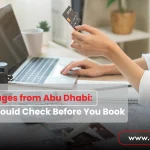 A woman using a credit card and laptop to book travel packages from Abu Dhabi, with a camera and maps on the desk suggesting holiday planning.