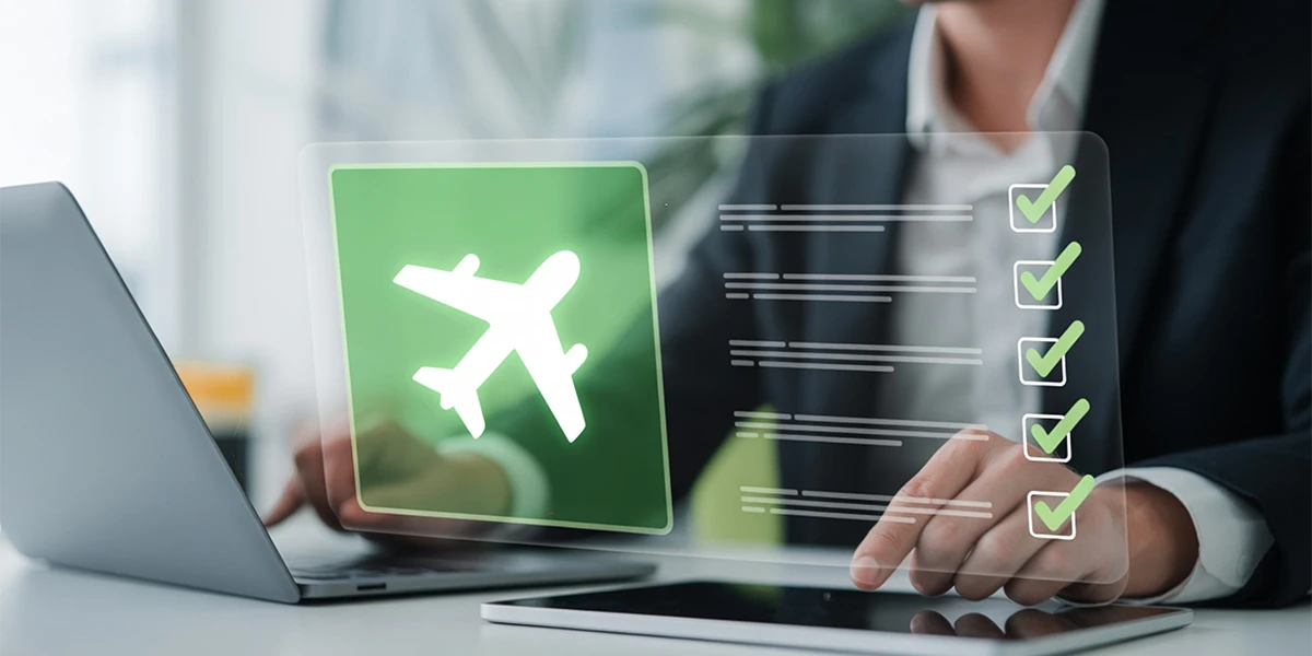 A businessman using a laptop and tablet with a digital interface showing an airplane icon and a checklist for corporate flight booking management.